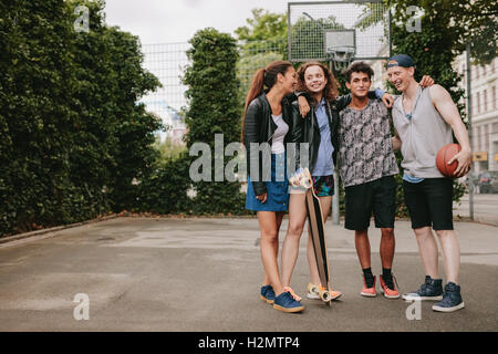 Full Length portrait of teenage friends standing avec skateboard et le basket-ball. Mixed Race groupe de personnes bénéficiant d'or Banque D'Images