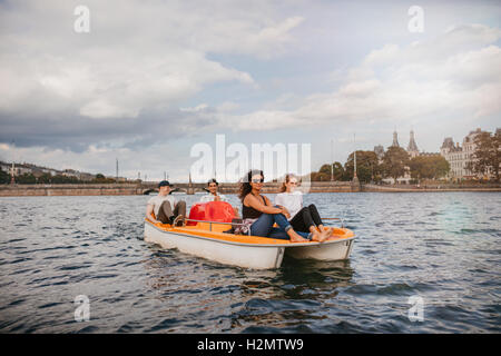 Tourné de quatre jeunes gens sur le lac en pédalo. Les femmes assises à l'avant avec des hommes à l'arrière du bateau de pédalage. Banque D'Images