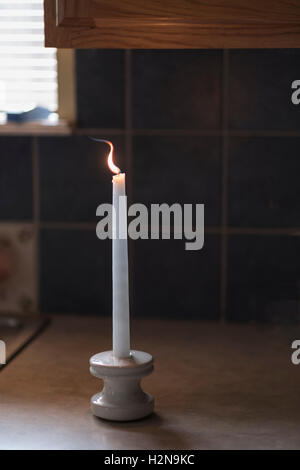 Une bougie blanche avec flamme, sur un comptoir de cuisine. Banque D'Images