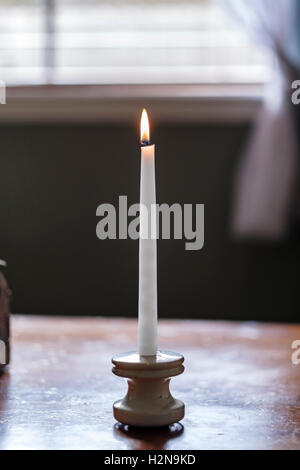 Une bougie blanche avec flamme assis sur une table. Banque D'Images