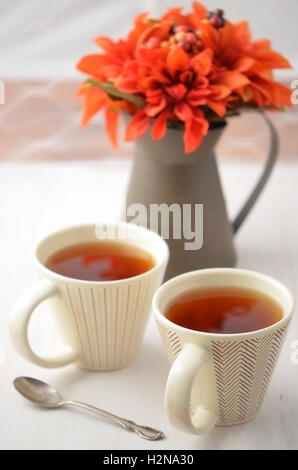 Deux tasses de thé chaud avec des fleurs d'automne en pichet rustique en format vertical Banque D'Images