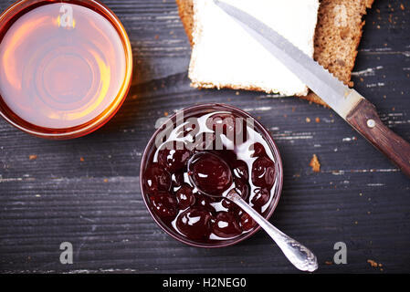 Tranche de pain avec beurre et confiture de cerise avec une tasse de thé sur un fond de bois noir. Vue d'en haut Banque D'Images