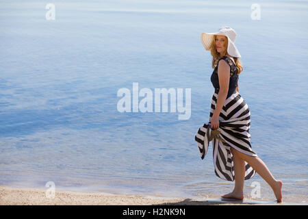 Belle femme dans un noir et blanc robe-soleil à marcher le long de la plage. Banque D'Images