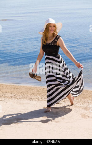 Belle femme dans un noir et blanc robe-soleil à marcher le long de la plage. Banque D'Images