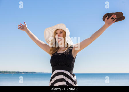 Belle femme dans un noir et blanc robe-soleil à marcher le long de la plage. Banque D'Images