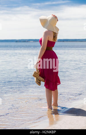 Belle femme avec un soleil rouge robe de marcher le long de la plage Banque D'Images