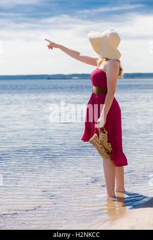 Belle femme avec un soleil rouge robe de marcher le long de la plage Banque D'Images