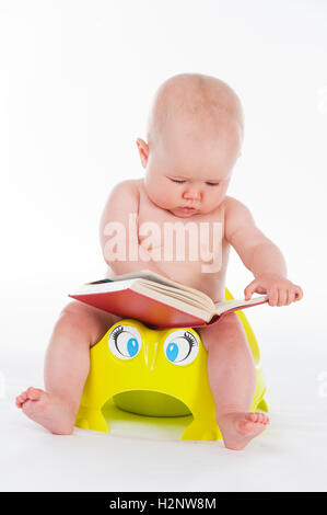 Bébé, 10 mois, assise avec un livre sur un pot Banque D'Images