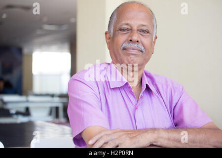 Closeup portrait portrait de monsieur âgé les bras croisés, plié en chemise rose, souriant, assis à l'intérieur de contenu isolé Banque D'Images