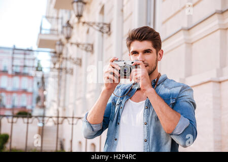 Beau jeune homme concentré en tenant avec pistures vieille photo appareil photo dans la ville Banque D'Images