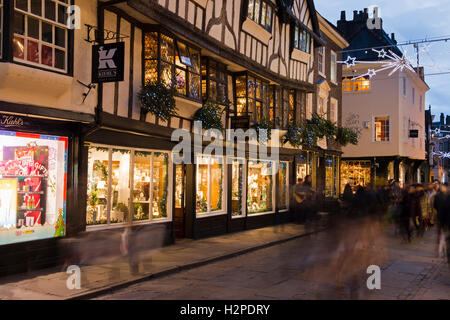 Sur une sombre soirée d'hiver, les acheteurs de Noël passent dans un flou de mouvement - une ambiance festive illuminée, Stonegate, York, Angleterre. Banque D'Images