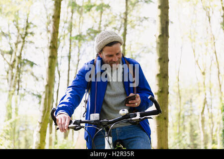 Man mountain biking texting with cell phone in woods Banque D'Images