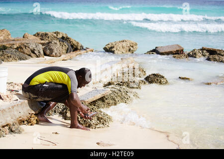 La Barbade Hastings Bay Fisherman jeune homme noir garçon sur la plage de pêche des autochtones pauvres mer ordures délabré délabrés privés pers Banque D'Images