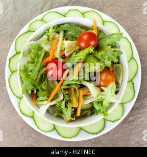 Bol de salade avec la tomate et la carotte à l'intérieur d'un anneau plaqué en plongée des concombres Banque D'Images