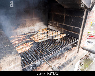Les sardines grillées sur un barbecue des. Une grille pleine de sardines de cuisson ou de maquereau cuit sur un barbecue en brique sur un charbon de bois chaud Banque D'Images