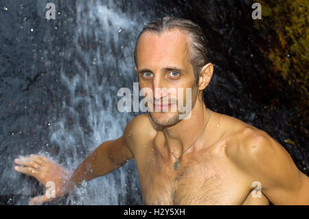 Un homme de prendre une douche relaxante sous une cascade à l'extérieur Banque D'Images