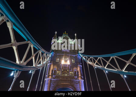 Jusqu'à la lumineuse entre éléments de la chaîne d'acier d'une tour de la Tower Bridge sur la Tamise contre le ciel nocturne, London, UK Banque D'Images