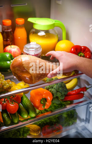 Des mains d'atteindre pour la cuisse de dinde dans la nuit dans le réfrigérateur ouvert Banque D'Images