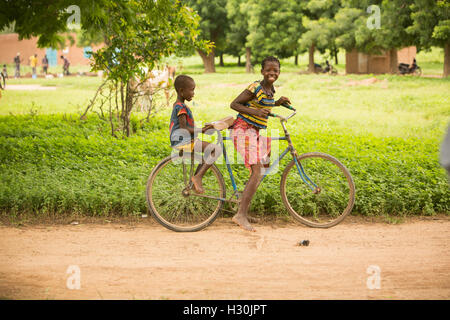 Des enfants heureux de rouler à bicyclette dans les régions rurales de Réo, Burkina Faso, du Département Afrique de l'Ouest. Banque D'Images