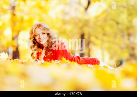 Belle jeune femme portant sur des feuilles jaunes en automne park Banque D'Images