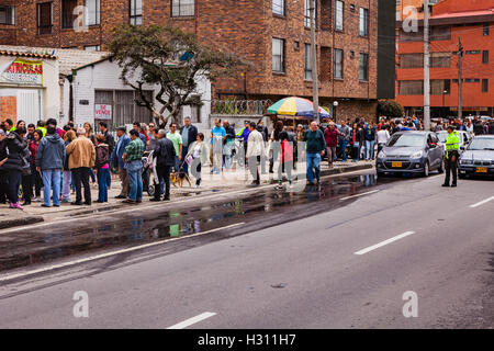 Bogota, Colombie - Octobre 02, 2016 : Les électeurs la queue pour entrer dans un bureau de scrutin sur Carrera 9, dans la capitale des Andes de Bogota, dans le pays de l'Amérique du Sud de la Colombie, au vote sur le référendum historique de paix. Un policier a arrêté le trafic afin de permettre aux électeurs de traverser la route. Photo prise dans l'après-midi du soleil. Format horizontal. Banque D'Images