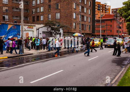 Bogota, Colombie - Octobre 02, 2016 : les électeurs en file d'attente pour entrer dans un bureau de scrutin sur Carrera 9, dans la capitale des Andes de Bogota, dans le pays de l'Amérique du Sud de la Colombie, au vote sur le référendum historique sur le processus de paix avec les FARC. À gauche derrière le peuple fait partie d'une fresque peinte dans les couleurs vives de l'Amérique latine, consacré au processus de paix. Un policier a arrêté le trafic afin d'aider les gens à traverser la route en toute sécurité. Banque D'Images