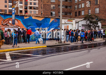 Bogota, Colombie - Octobre 02, 2016 : les électeurs en file d'attente sur la droite, pour entrer dans un bureau de scrutin sur Carrera 9, dans la capitale des Andes de Bogota, dans le pays de l'Amérique du Sud de la Colombie, au vote sur le référendum historique sur le processus de paix avec les FARC.à gauche, derrière le peuple fait partie d'une fresque peinte dans les couleurs vives de l'Amérique latine, dédiée au processus de paix ; la parole, Paz, Espagnol pour la paix, est partiellement visible. Banque D'Images