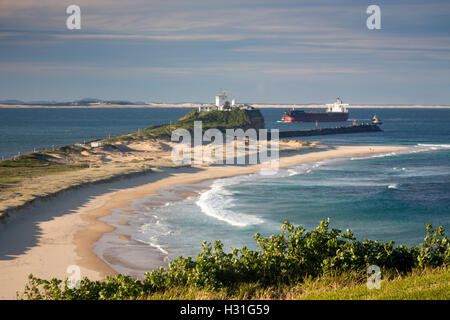 Plage de Nobbys et phare avec navire sera guidée par des remorqueurs par estuaire de Hunter River Newcastle NSW Australie Banque D'Images