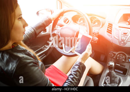 Jeune femme en robe rouge dans la voiture et holding smartphone Banque D'Images