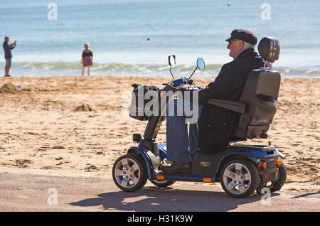 Un homme âgé sur Colt fierté scooter de mobilité le soleil brille sur la plage de Bournemouth en Octobre Banque D'Images