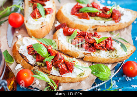 Bruschetta au fromage à la crème, le pesto, basilic frais et tomates séchées au soleil sur une table en bois rustique bleu Banque D'Images