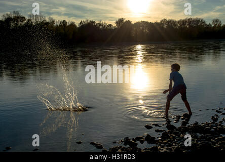 Garçon jette des pierres dans la rivière au coucher du soleil Banque D'Images