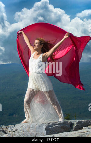 Danseuse en robe blanche tissu rouge ondulant dans le vent au sommet de Mt. Kearsarge, NH. Banque D'Images