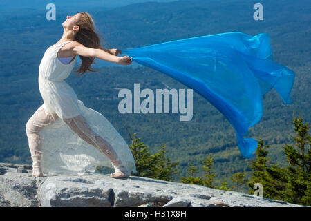 Danseuse en robe blanche danse avec tissu bleu dans le vent au sommet de Mt. Kearsarge, New Hampshire. Banque D'Images
