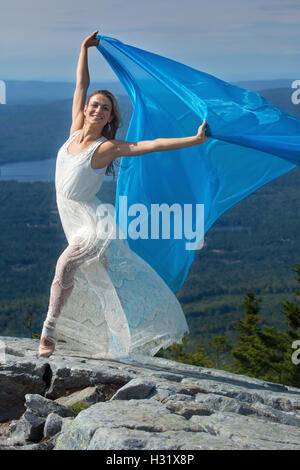 Danseuse en robe blanche danse avec tissu bleu dans le vent au sommet de Mt. Kearsarge, New Hampshire. Banque D'Images