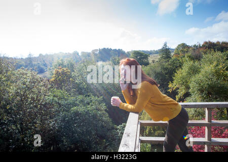 Jeune femme appuyée sur son balcon dans son gardenw hilst en utilisant son téléphone. Banque D'Images