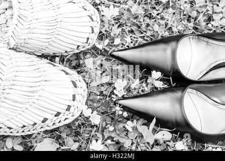 Chaussures noires et de paille tissée chaussons sur l'herbe comme métaphore sur la ville et la campagne, en noir et blanc Banque D'Images