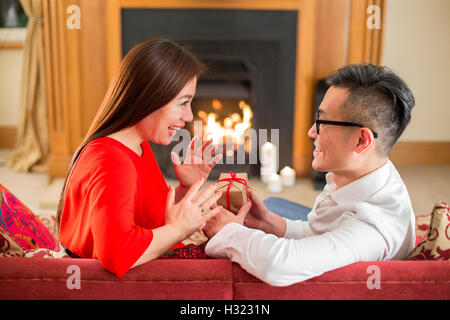 Couple chinois assis dans leur maison. L'homme remet un cadeau à son partenaire, qui est à la recherche avec excitation à lui. Banque D'Images