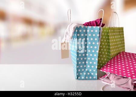 Trois sacs en papier pour l'achat de couleur avec des cercles blancs sur tableau blanc réfléchissant avec de nouveaux vêtements à l'intérieur dans un centre commercial. Face Banque D'Images