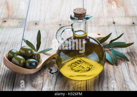 Une bouteille en verre d'huile d'olive et une cuillère en bois avec des olives sur une table Banque D'Images