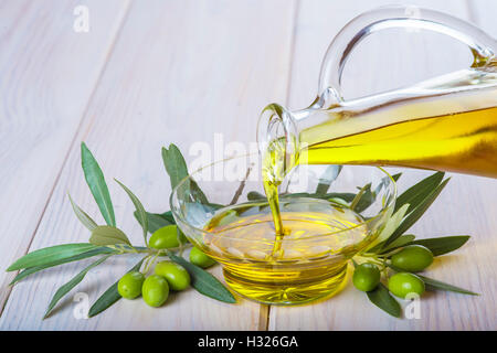 Verser la bouteille de l'huile d'olive vierge extra dans un bol en verre Banque D'Images