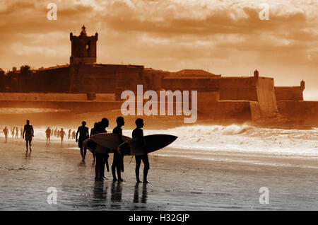 Silhouette de surfeurs à la plage face à la mer au coucher du soleil Banque D'Images