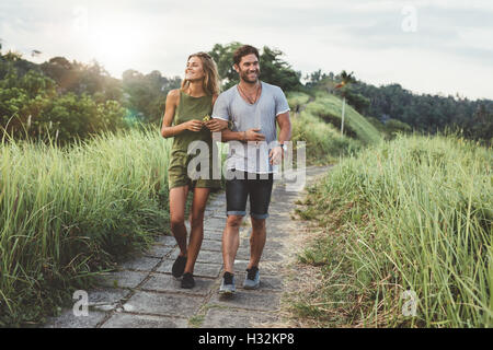 Piscine shot of young couple in love marche sur chemin par grass field. L'homme et de la femme marchant le long tall grass field. Banque D'Images