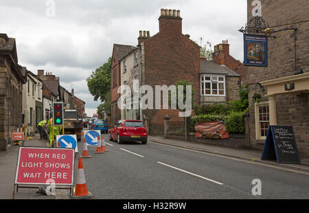 Travaux en étroite bordée de bâtiments en briques historique village anglais de Belper avec feux de circulation, panneaux, et des voitures Banque D'Images