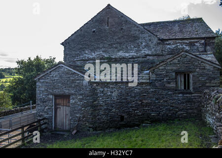 Un très vieux bâtiment de ferme en pierre avec des fenêtres cassées et des portes en bois. Banque D'Images