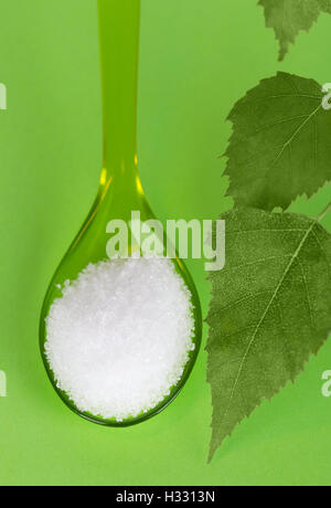 Le xylitol sucre de bouleau sur cuillère en plastique avec des feuilles de bouleau sur vert. L'alcool du sucre blanc cristallisé, substitut utilisé comme édulcorant. Banque D'Images
