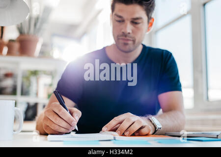 Jeune homme d'affaires d'écrire quelques notes importantes dans journal à son bureau. Jeune homme d'affaires personnelles ou sa mise à jour Banque D'Images