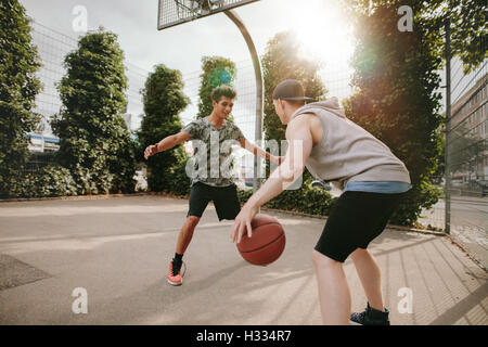 Jeunes amis jouant au basket-ball ensemble, garçon en face de blocage net et autres dribbler le ballon sur une cour. Banque D'Images