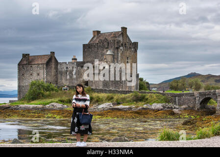 Tourisme d'Asie en tenant l'appareil photo de votre smartphone avec selfies sur stick selfies en face du château Eilean Donan Scottish Highlands, Ecosse Banque D'Images