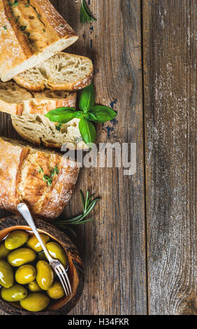 Olives vertes et des tranches de ciabatta sur fond de bois rustique Banque D'Images